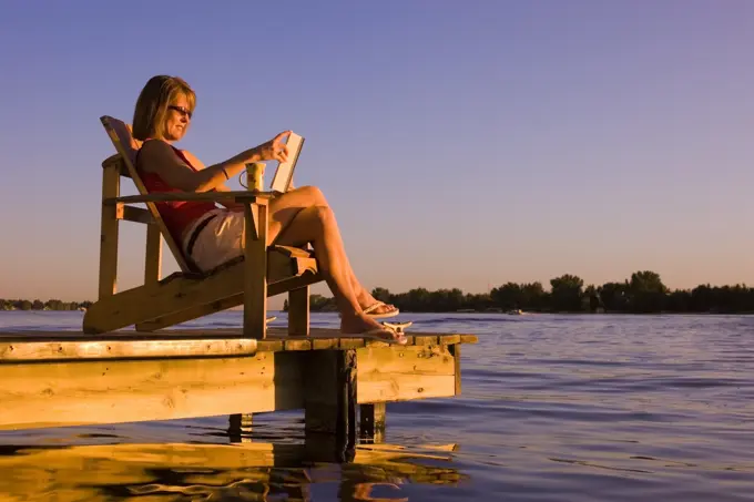 woman relaxing on dock at lake. Alberta, Canada.