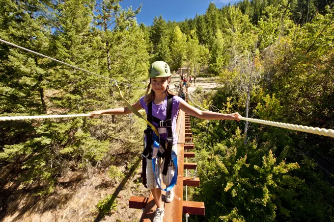 Young girl walks on suspension bridge at Oyama Zipline, Okanagan Valley, BC, Canada.