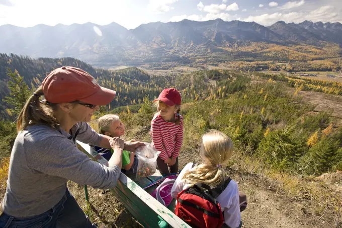 Woman with daughters relax on bench during hiking on Castle Mountain Trail in autumn, Fernie, BC, Canada.