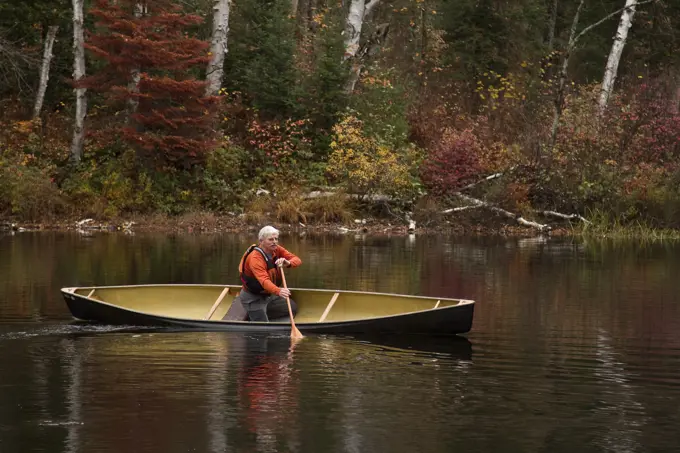 Elderly man paddling canoe in serene setting on Oxtongue Lake, Muskoka, Ontario, Canada.