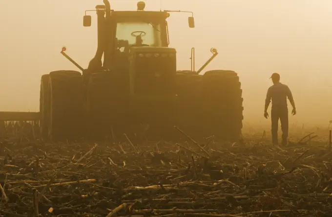 a farmer walks toward a tractor pulling cultivating equipment in a sunflower stubble field, near Lorette, Manitoba, Canada