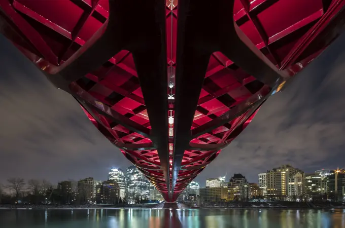 Pedestrian Peace Bridge and Downtown Calgary reflecting in the Bow River at night. Calgary, Alberta, Canada.