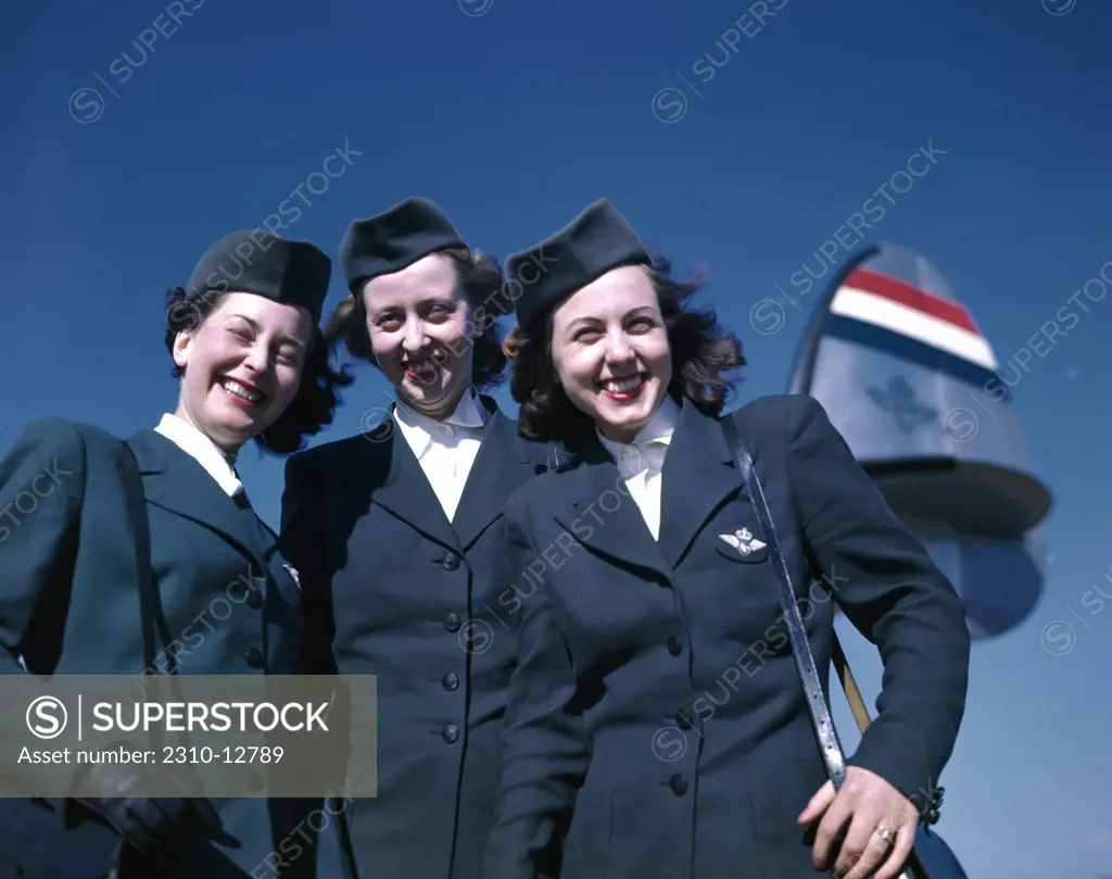 Portrait of three of three female cabin crew members standing near airplane against blue sky