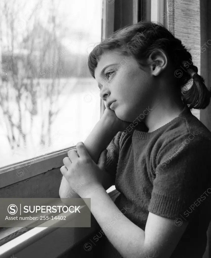 Melancholic girl looking through window