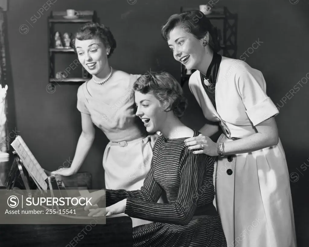 Side profile of a young woman playing the piano with two young women standing behind her