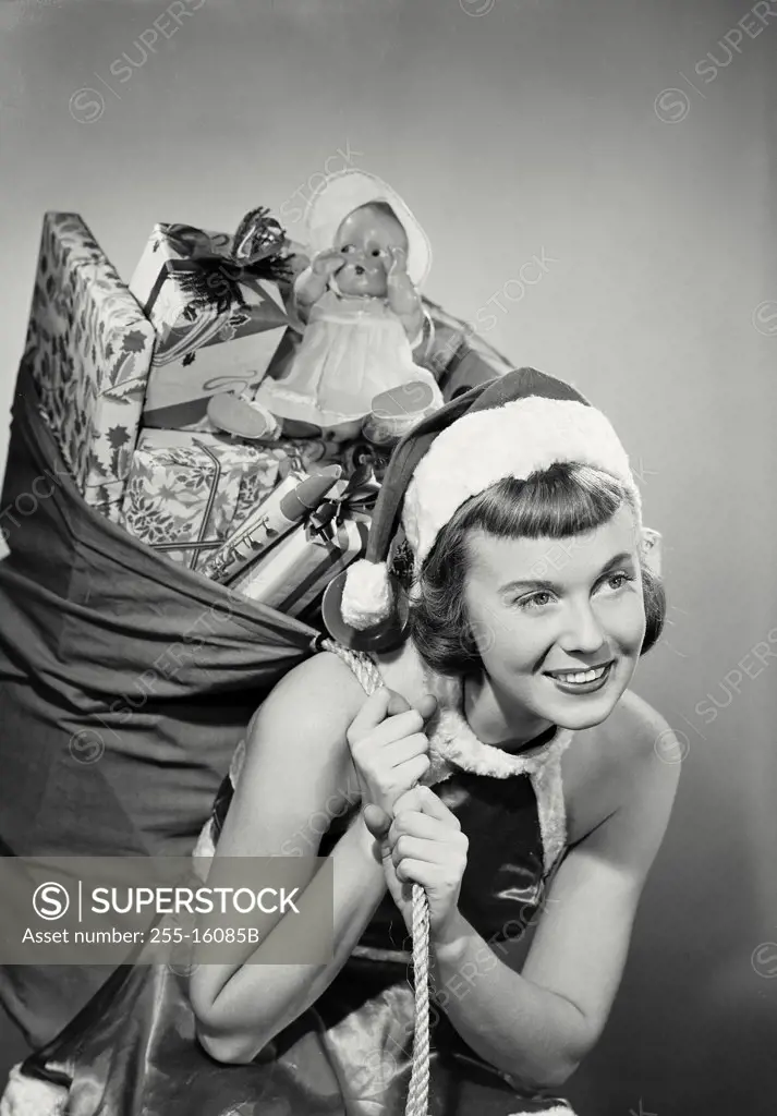 Vintage photograph. Close-up of a young woman dressed as santa with toy sack over shoulder