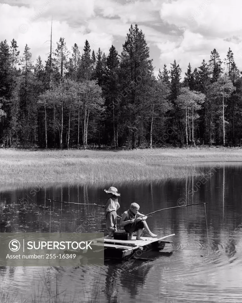 Vintage photograph of boy and girl sitting on wooden raft, fly-fishing with improvised fishing rods on lake