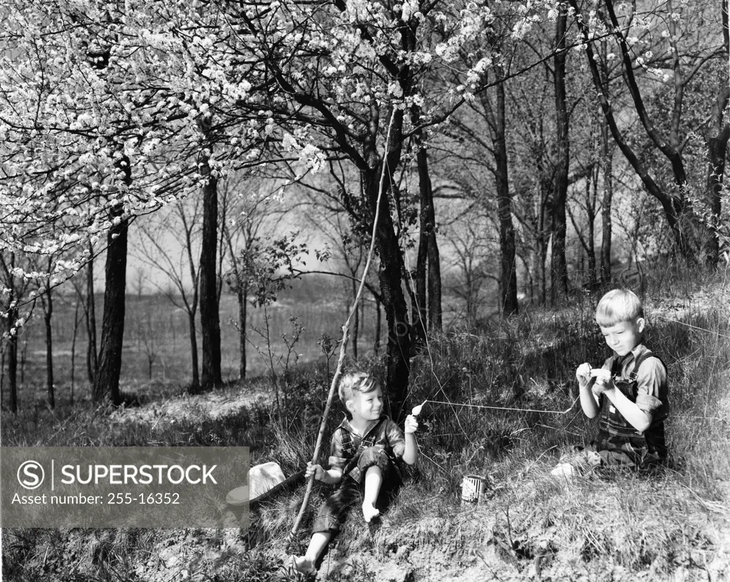 Vintage photograph of boys with improvised fishing rod putting bait on hook