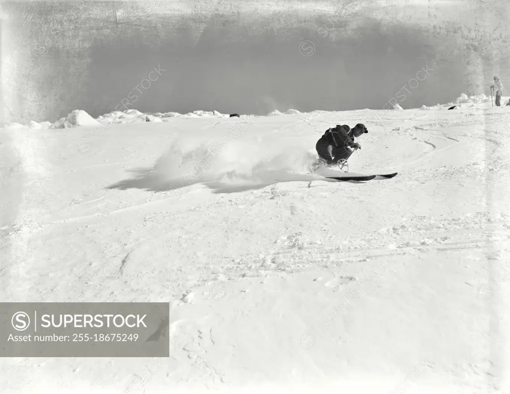 Vintage photograph. Skiing at the spring ski center on Mt. Washington, New Hampshire. Skier making a high-speed Christiana turn on a steep slope. Snow spraying behind him. 