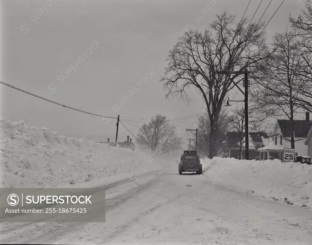 Vintage photograph. Car on road, winter scene in Gorham, New Hampshire. Snowstorm and high snow banks.