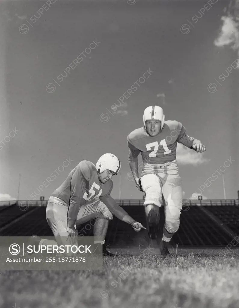 Vintage photograph. Football players - Kicker running up to holder to kick football. Models released