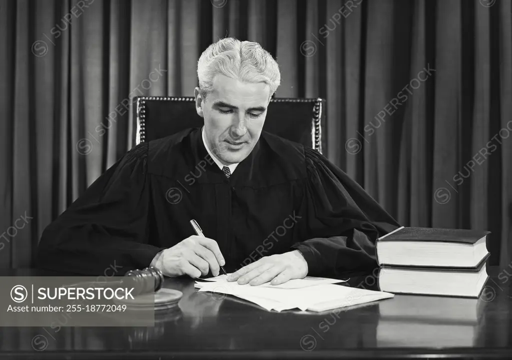 Vintage photograph. Male judge sitting at desk writing on paper. Model released.