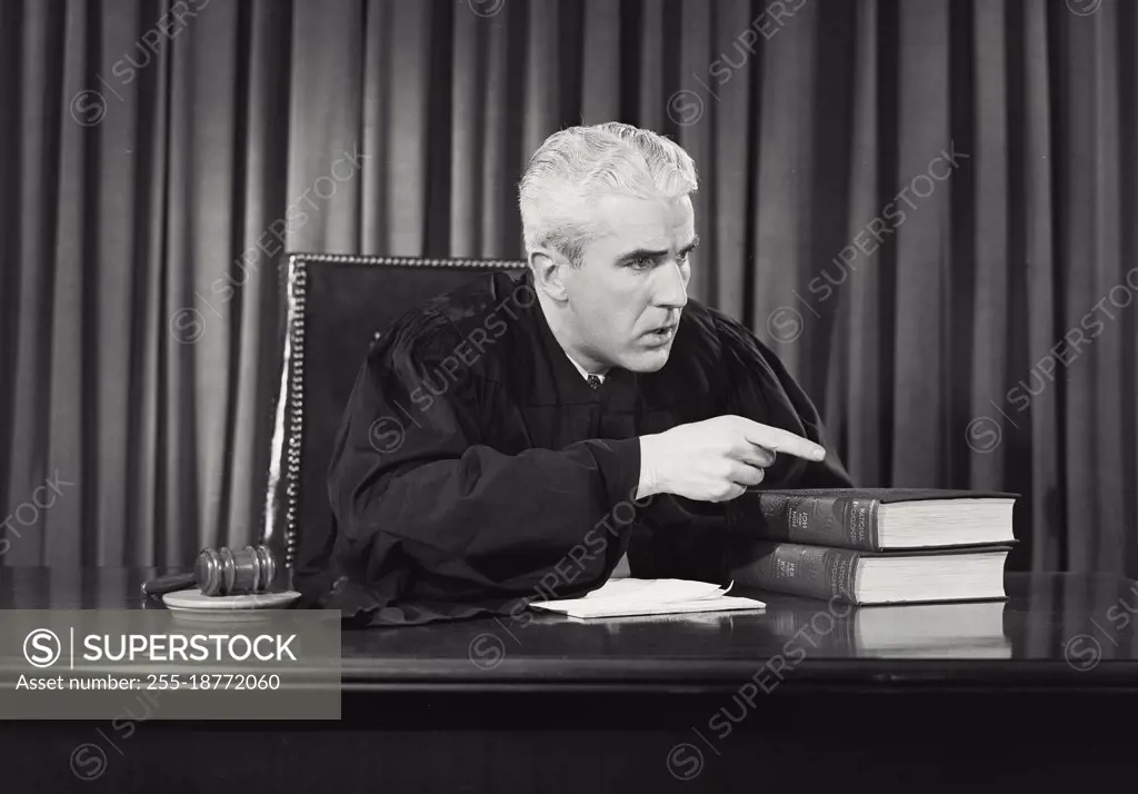 Vintage photograph. Male judge sitting at desk looking stern and pointing off camera. Model released.