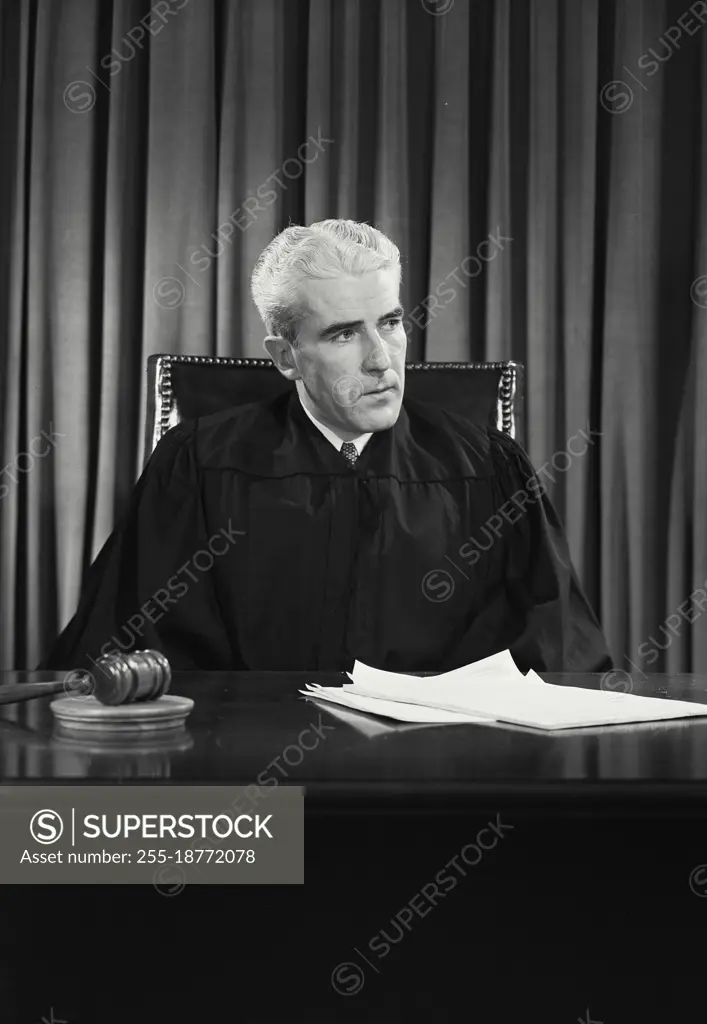 Vintage photograph. Male judge sitting at desk looking thoughtful. Model released.