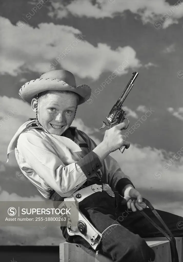 Vintage photograph. Young boy and cowboy outfit position to be riding horse holding gun