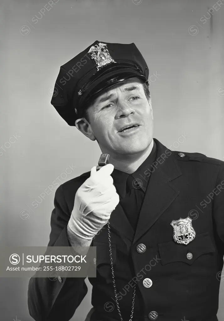 Vintage photograph. Policeman holding up whistle in gloved hand with grin