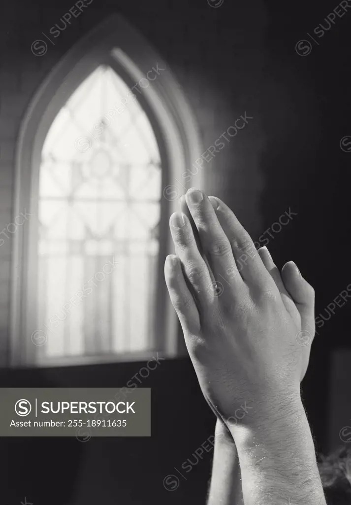 Vintage photograph. Hands clasped in prayer in front of church window