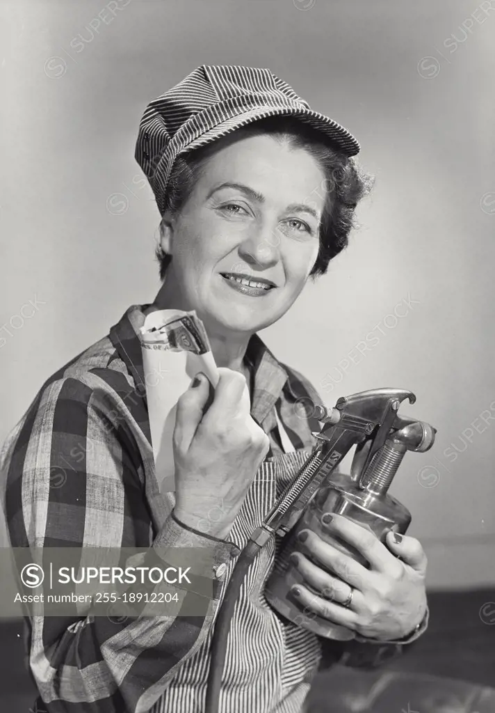 Vintage photograph. Middle aged woman dressed in work uniform holding paint sprayer and envelope of money