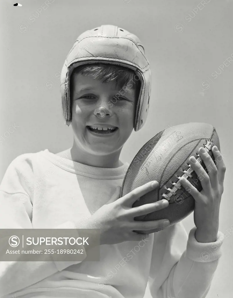 Vintage photograph. Portrait of smiling boy wearing football helmet holding up football