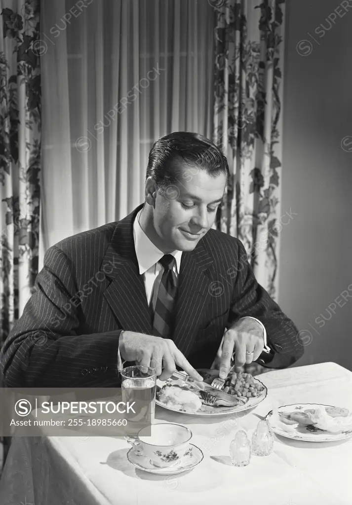 Vintage photograph. Man at table cutting food on plate.