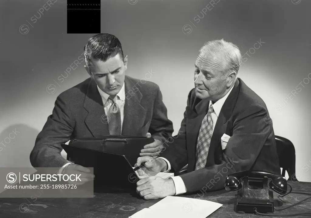 Vintage photograph. young man and older man sitting together at desk discussing papers