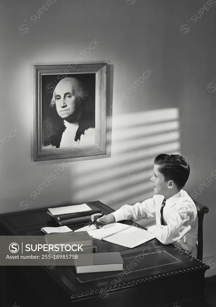 Vintage photograph. young boy sitting at desk looking at painting of George Washington.