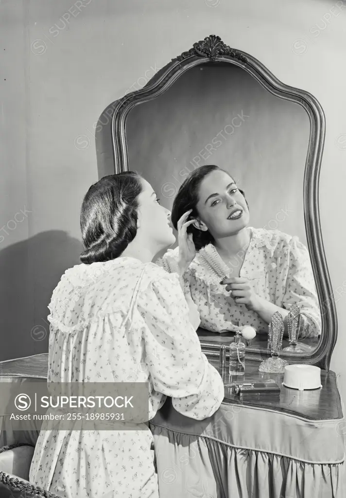 Vintage photograph. Woman in night gown adjusting hair in mirror.