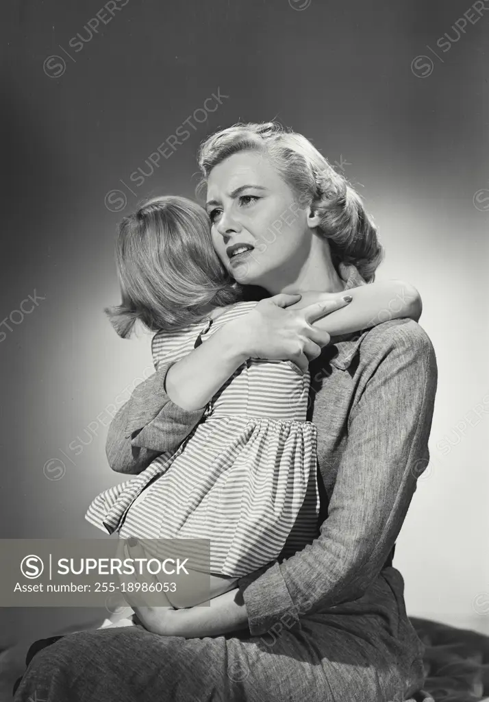 Vintage photograph. Mother hugging young daughter in lap with worried expression