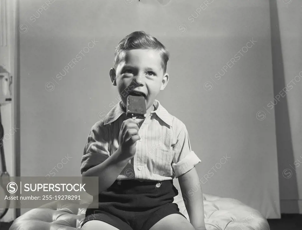 Vintage photograph. Little boy taking bite out of ice cream pop.