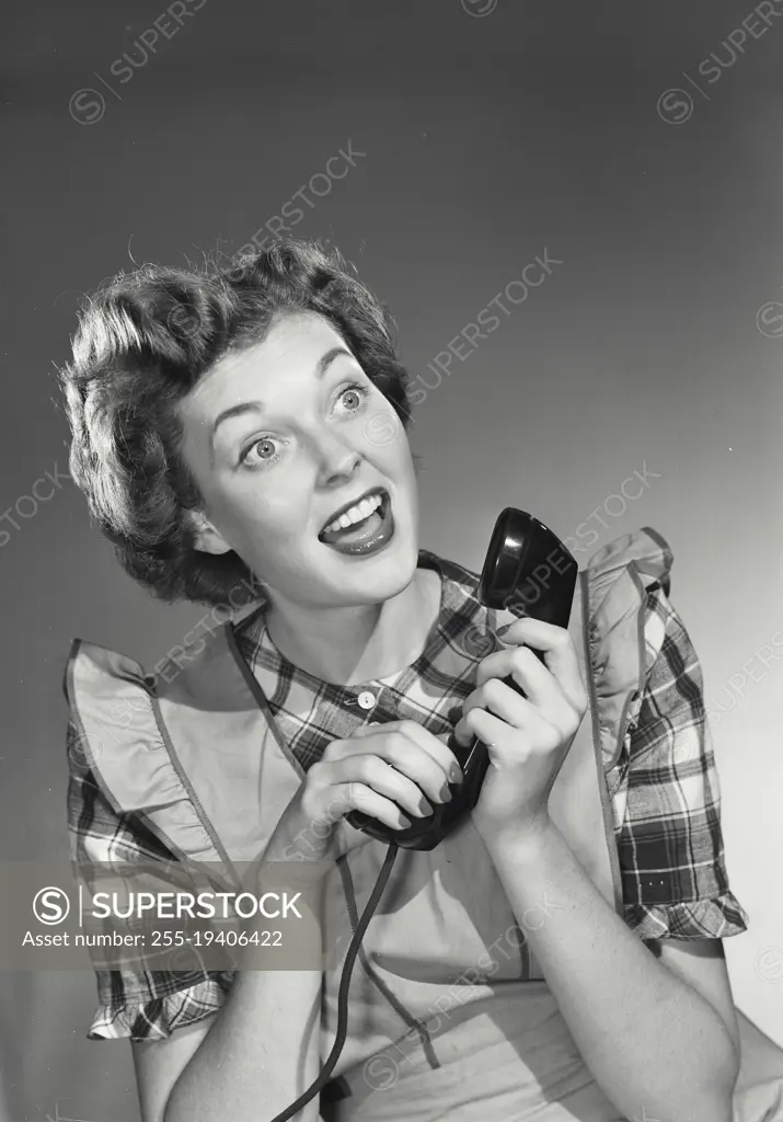 Vintage photograph. Woman in apron holding phone call with excited expression.