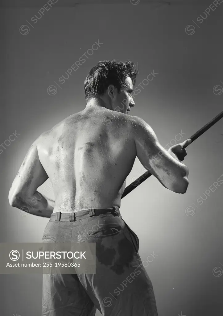 Vintage photograph. Back view of shirtless man holding pipe