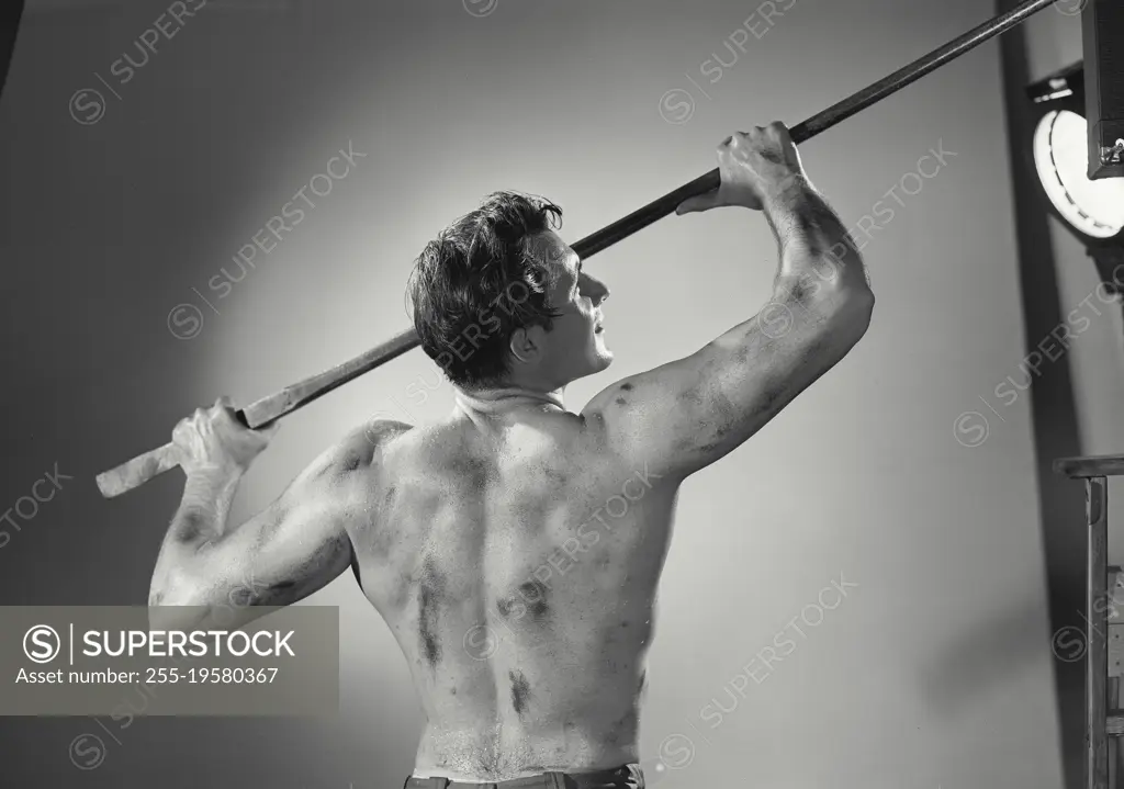 Vintage photograph. Back view of shirtless man holding tool