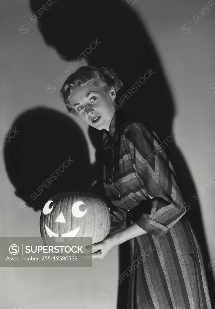 Vintage photograph. Woman holding Jack o' Lantern with shadow on wall