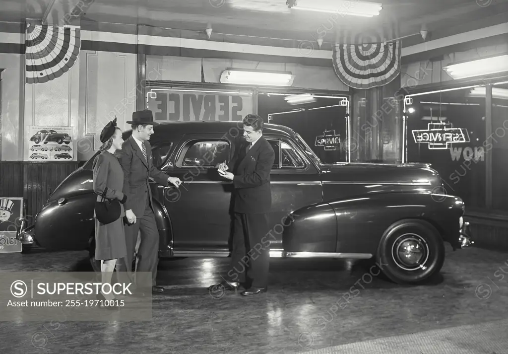 Vintage photograph. Couple in car dealership standing next to Chevrolet Stylemaster talking to salesman