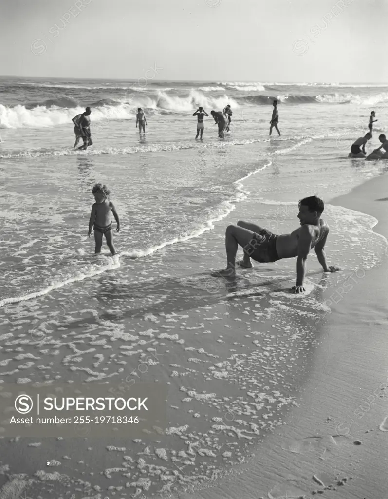 Vintage photograph. Boy crab-walking at beach with younger boy watching