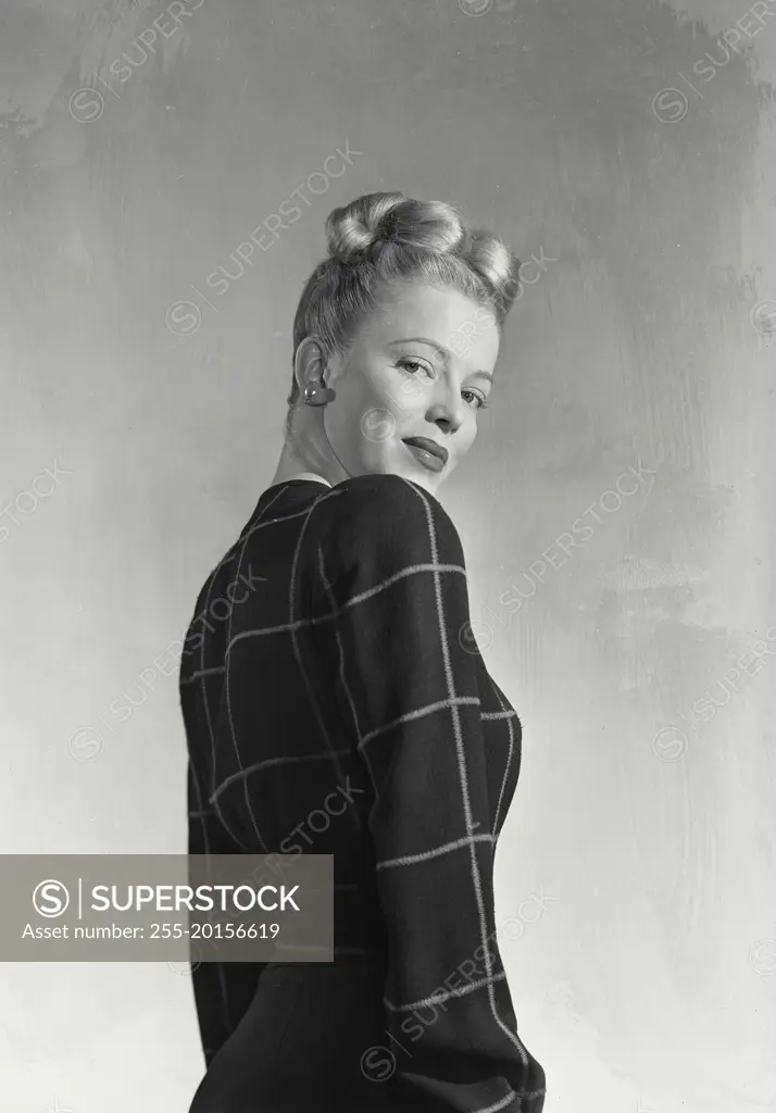 Vintage photograph. Blonde woman with hair in up style wearing dark blouse turned to side smiling