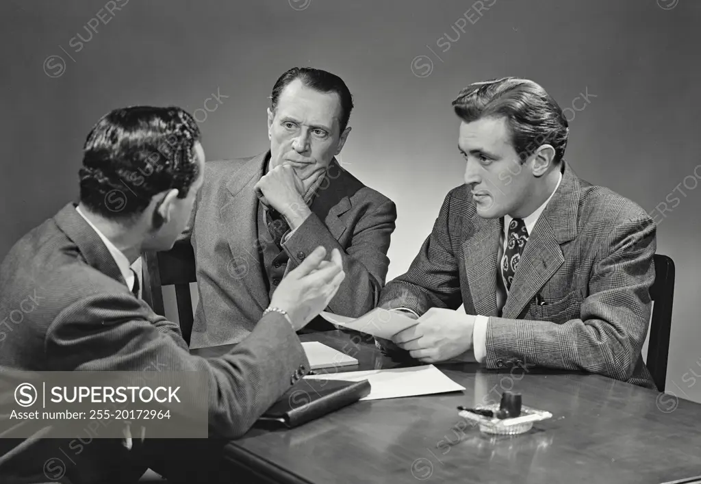 Vintage photograph. Group of men in suits sitting at desk having business discussion