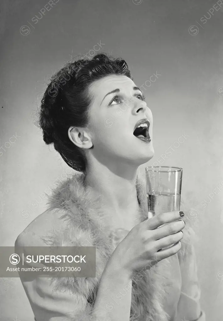 Vintage photograph. Woman holding glass with mouth open looking above