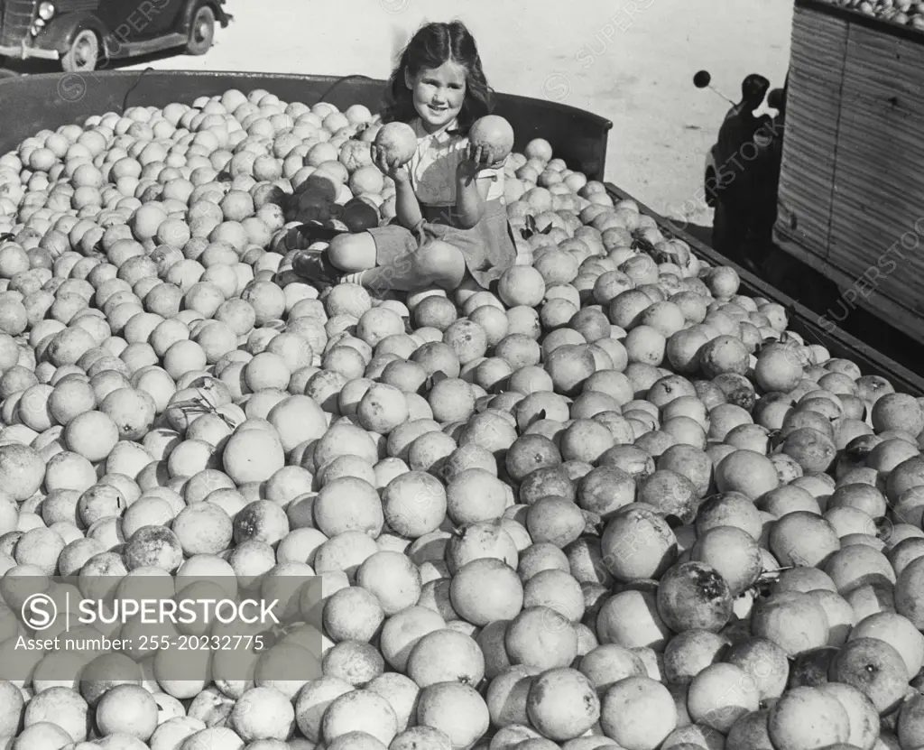 Young girl sitting in the middle of 24,000 pounds of grapefruits, ready to be canned and shipped all over the world