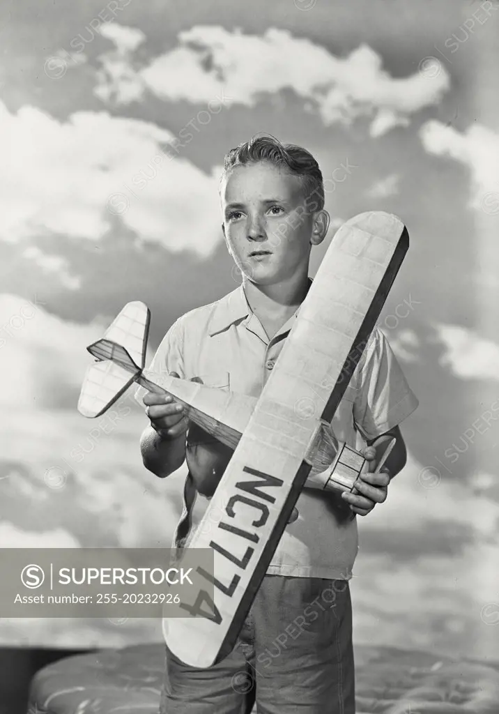 Boy standing with model airplane in front of cloud sky background