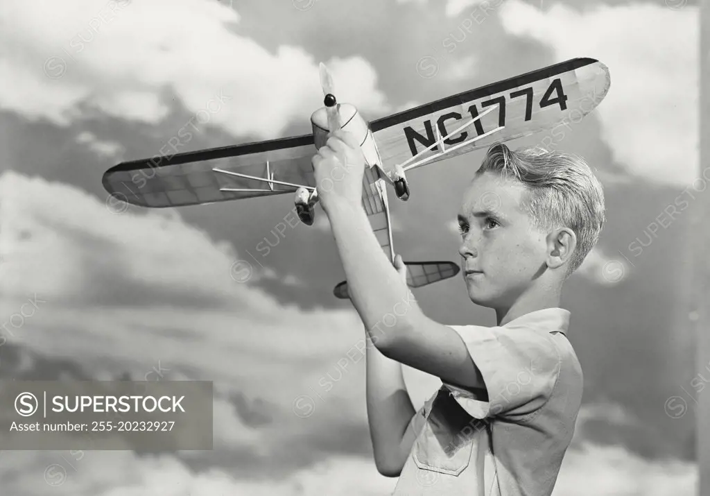 Boy spinning propeller on toy airplane in front of cloud sky background