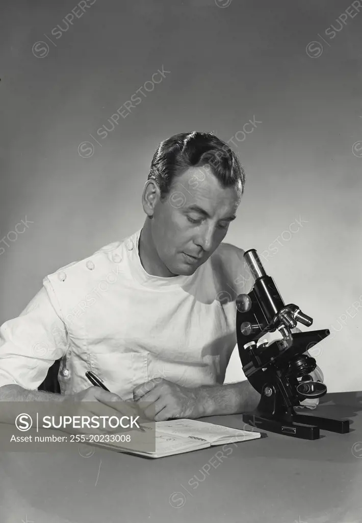 Scientist using notebook while at microscope