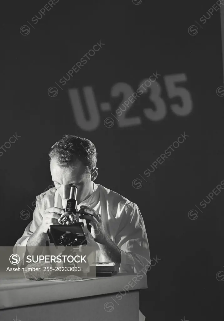 Scientist looking through microscope with U-235 (Uranium Isotope) being projected on the wall