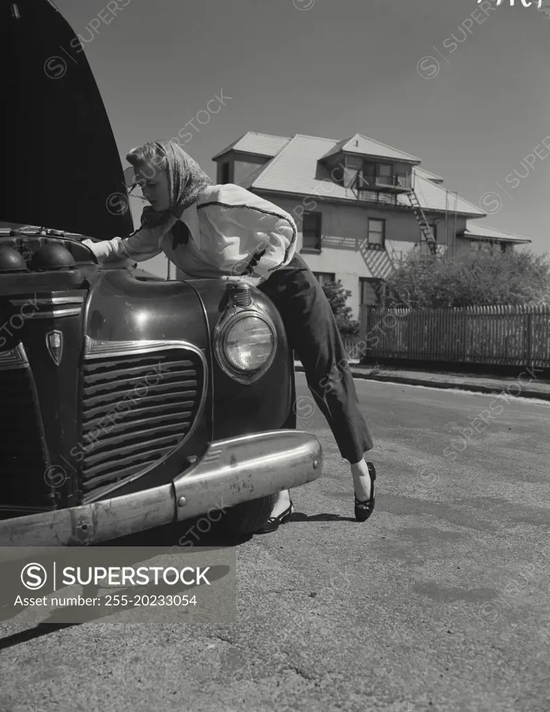 Woman inspecting under the hood of car.