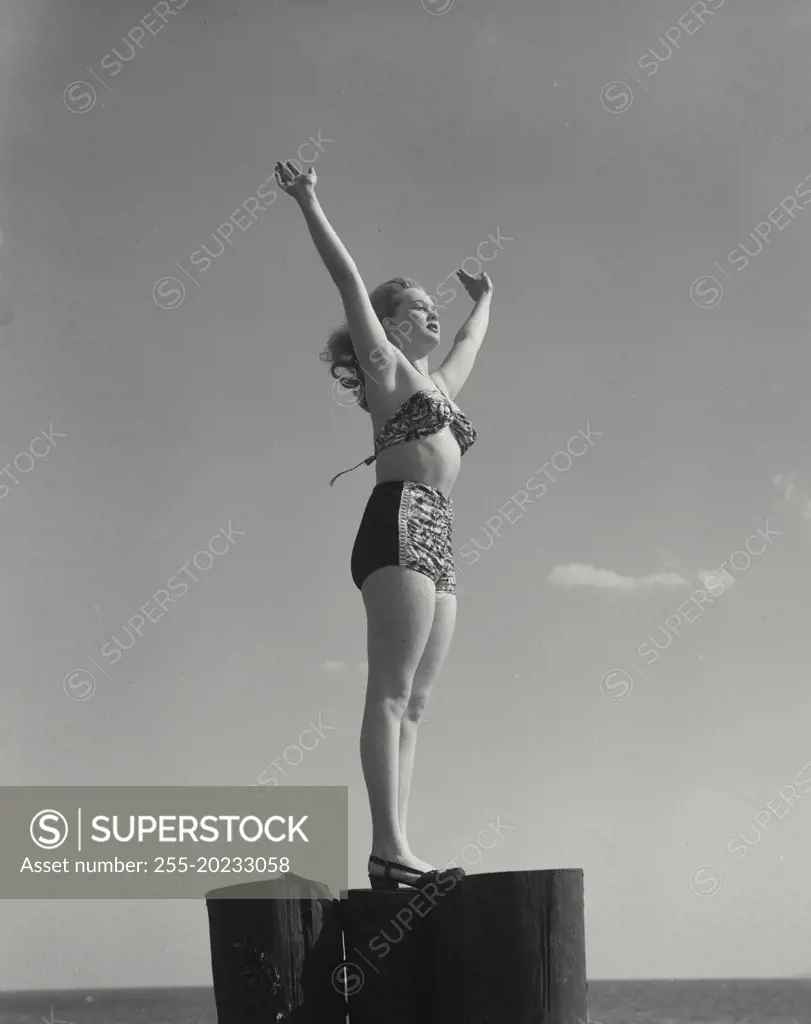 Woman in swimsuit standing on post with hands in air