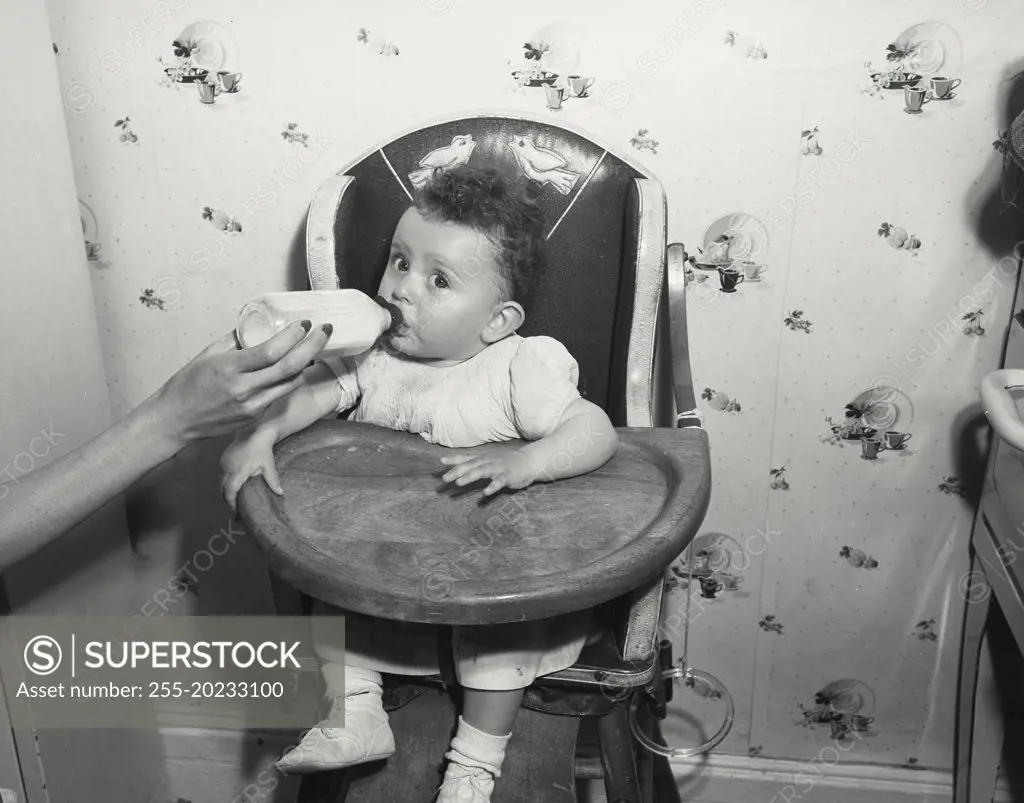 Baby in high chair drinking from bottle