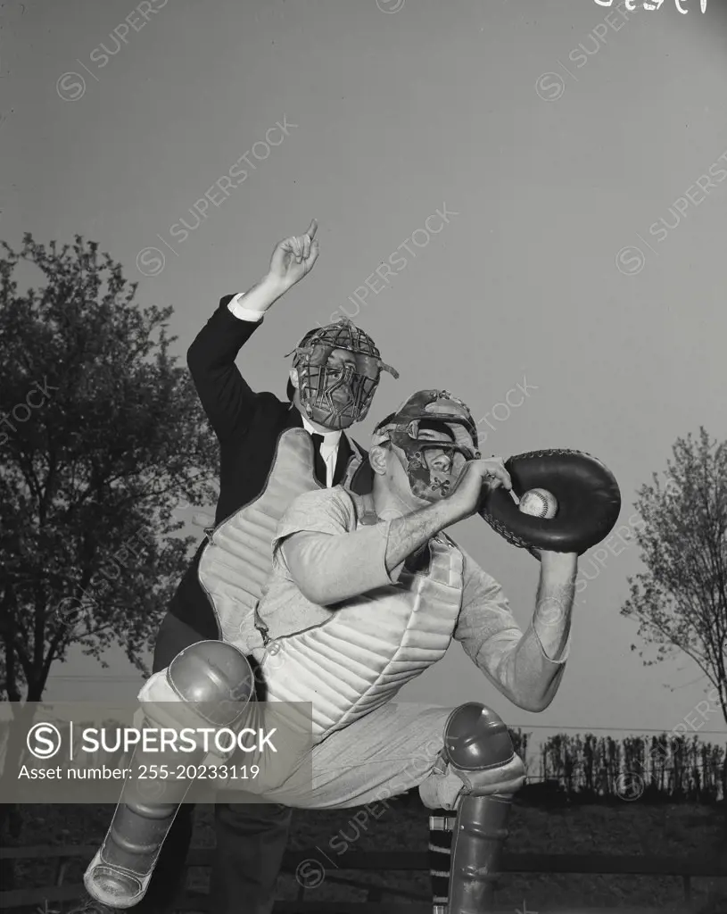 Baseball catcher with ball in mitt and umpire standing above