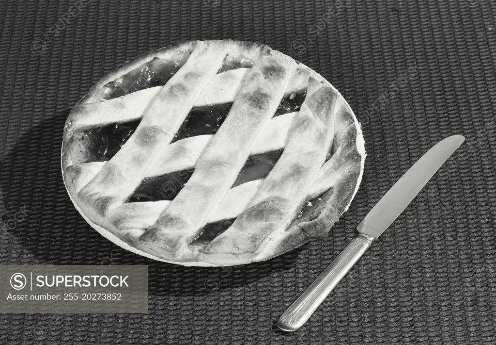 Vintage photograph. Pie with woven crust sitting on table with knife