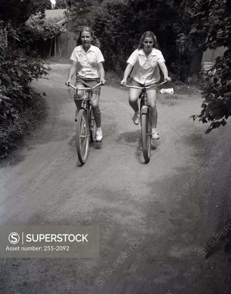 Two teenage girls riding bikes on dirt track