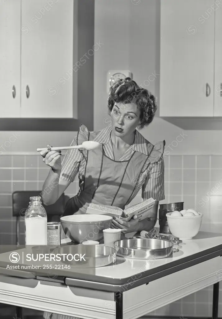 Vintage photograph. Mid adult woman preparing food with the help of a cookbook